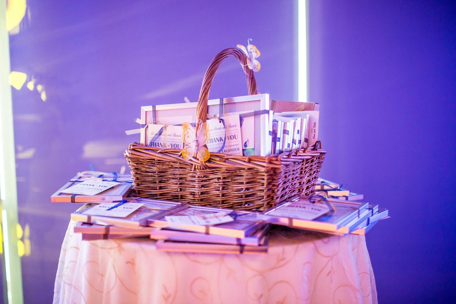A beautifully arranged gift basket on a round table, illuminated by purple lighting for an elegant event setup.